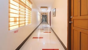 A hotel corridor with a fire exit sign, wooden doors, and a tiled floor. - RedDoorz Premium @ Nick Hotel Gerona Tarlac (Gerona)