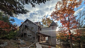 A rustic log cabin with a steep staircase, a stone tower, and a wooden deck leading to the entrance. - Oceanfront Cabin-Castle in Maine Woods (Georgetown)