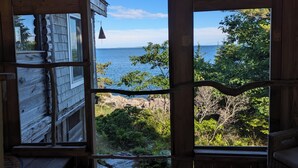 A wooden cabin with a large window overlooking a rocky shoreline and the sea. - Oceanfront Cabin-Castle in Maine Woods (Georgetown)