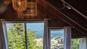 A room with a large window overlooking a rocky coastline and greenery. - Oceanfront Cabin-Castle in Maine Woods (Georgetown)
