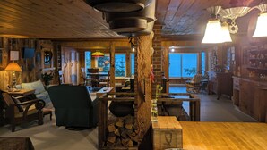 A rustic cabin interior with a wooden dining area, a fireplace, and a view of the outdoors. - Oceanfront Cabin-Castle in Maine Woods (Georgetown)