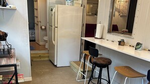 Cocina compacta con refrigerador, lavamanos y un taburete de bar.