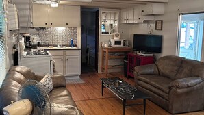 Una sala de estar moderna con un sofá de cuero, una mesa de centro y un televisor. Cuenta con una zona de cocina con armarios y un microondas.