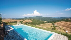 A swimming pool with a stone border, surrounded by a stone deck, overlooking a valley with hills and a clear blue sky. - Refined Home W/ Pool, Stunning View, and Relaxing (Volterra)