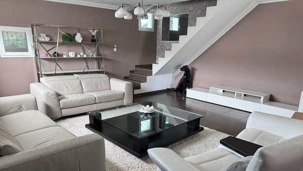 Un salon moderne avec un escalier, des canapés blancs, une table basse en verre et une décoration minimaliste.