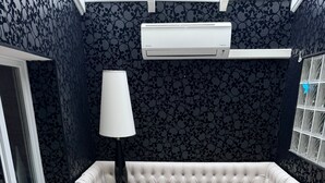 Une pièce avec un banc rembourré blanc, une table, une lampe et un mur orné d’un motif.