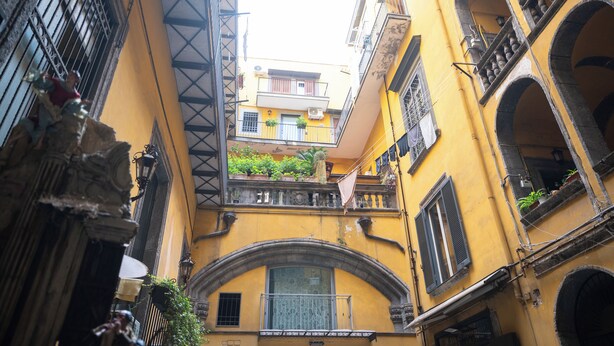 A narrow street with yellow buildings, balconies, and a mix of architectural styles. - Centro Storico Napoli • 2 Camere • Balcone • Famiglie e Gruppi (Napoli)