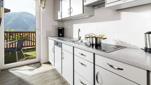 A modern kitchen with white cabinets, stainless steel appliances, and a view of mountains through a sliding glass door. - Ferienwohnung in Kurtatsch an der Weinstrasse (Kurtatsch)