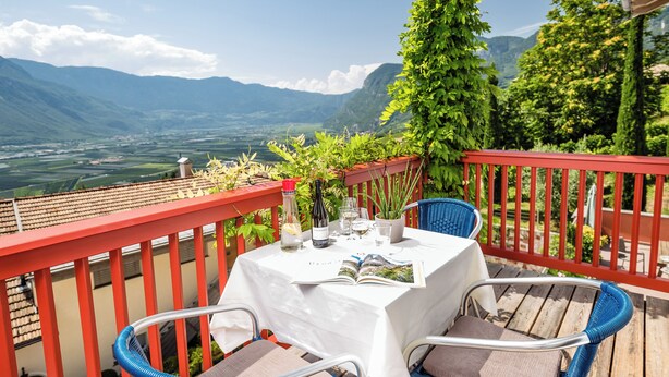 A table set on a balcony with a mountain view, a bottle of wine, and glasses. - Ferienwohnung in Kurtatsch an der Weinstrasse (Kurtatsch)