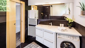 A modern bathroom with a built-in washing machine, a large mirror, and a towel rack. - Ferienwohnung in Kurtatsch an der Weinstrasse (Kurtatsch)