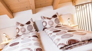 A hotel room with two beds, each with a patterned bedspread and matching pillows. There is a bedside table with a lamp on each side of the beds. - Ferienwohnung in Kurtatsch an der Weinstrasse (Kurtatsch)