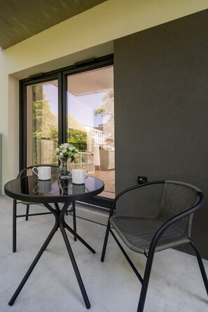 A balcony with a glass table and chairs, a vase with flowers, and a view of a building and trees. - Łódź Fabryczna Apt - Parking, Workspace, Balcony - by Rentujemy (Łódź)