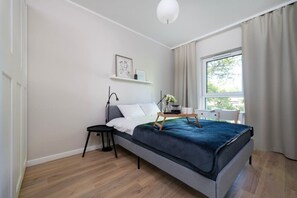 A modern bedroom with a bed, bedside table, and a window with curtains. - Łódź Fabryczna Apt - Parking, Workspace, Balcony - by Rentujemy (Łódź)