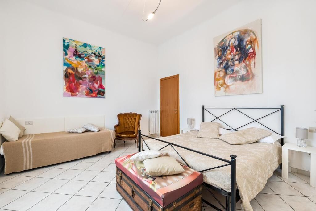 Une chambre à coucher comprenant un lit, un canapé, un fauteuil et deux tableaux abstraits accrochés aux murs.