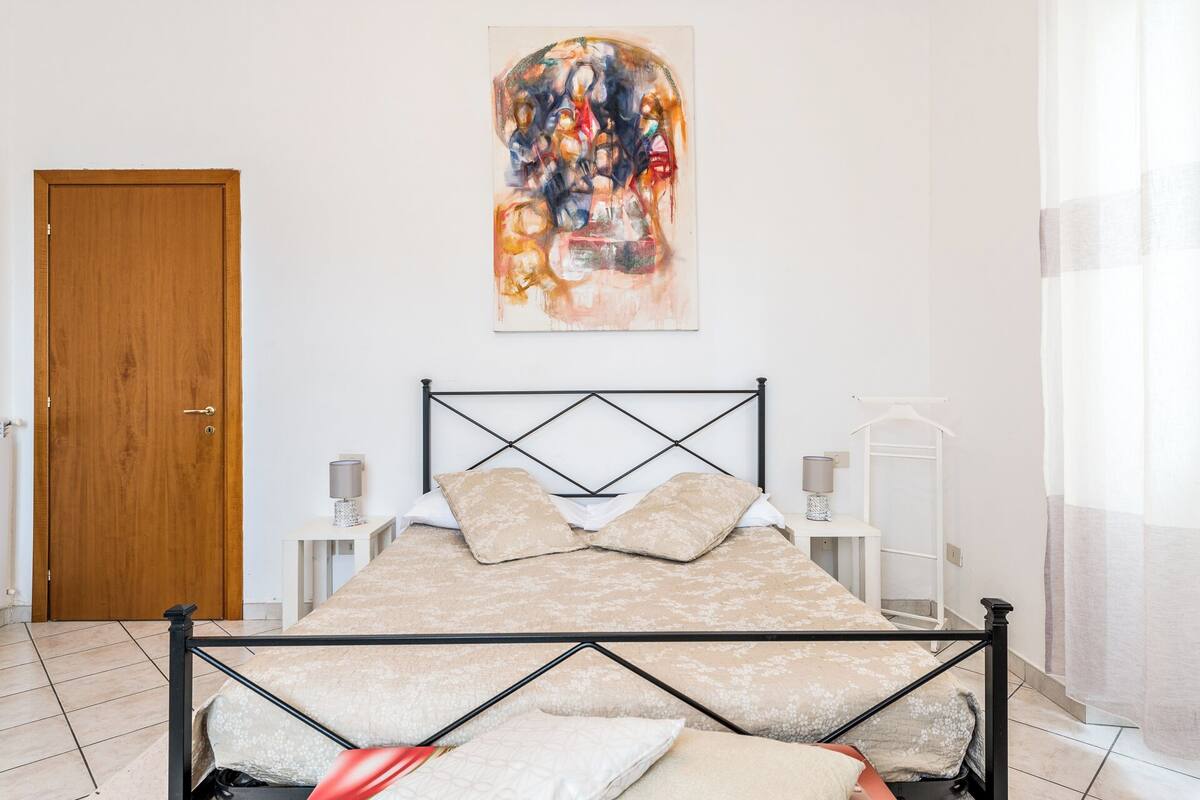 Une chambre à coucher avec un lit, une porte en bois, un tableau et une table de chevet avec une lampe.