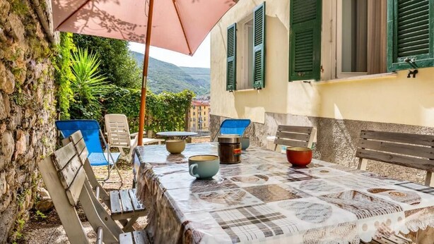 Een terras met een eettafel, omringd door stoelen en een parasol.