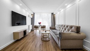 A modern living room with a sofa, a TV mounted on the wall, a dining table with chairs, and a window with curtains.