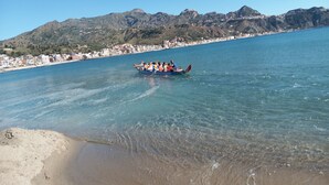 A dragon boat on a clear blue sea with a mountainous coastline in the background.