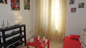 A living room with a red sofa, a black console table with decorative items, a red coffee table, and a window with a patterned curtain.