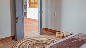 A bedroom with a bed, a patterned rug, a hanging light fixture, and an open door leading to another room. - Raizes AXM (Circasia)