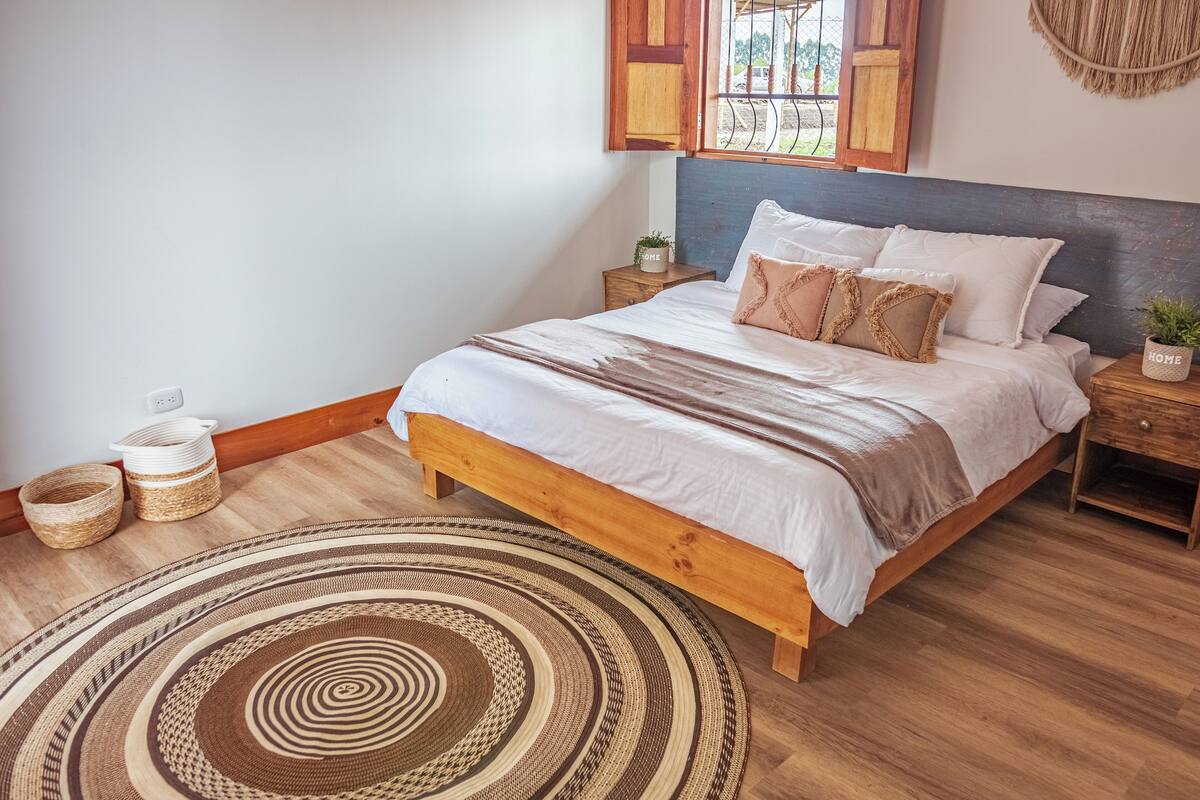 A bedroom with a wooden bed, a round woven rug, and a small potted plant on the nightstand.