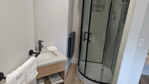A bathroom with a glass-enclosed shower, a sink with a towel, and a wooden shelf. - The Livery (Brockton)