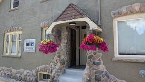 A building with a stone facade, a porch with steps, and flower baskets. - The Livery (Brockton)