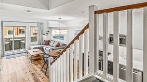 A modern living room with a wooden staircase, a sofa set, and a dining area. - Modern Penthouse, Breathtaking Views, Hot tub/Pool (Canmore)