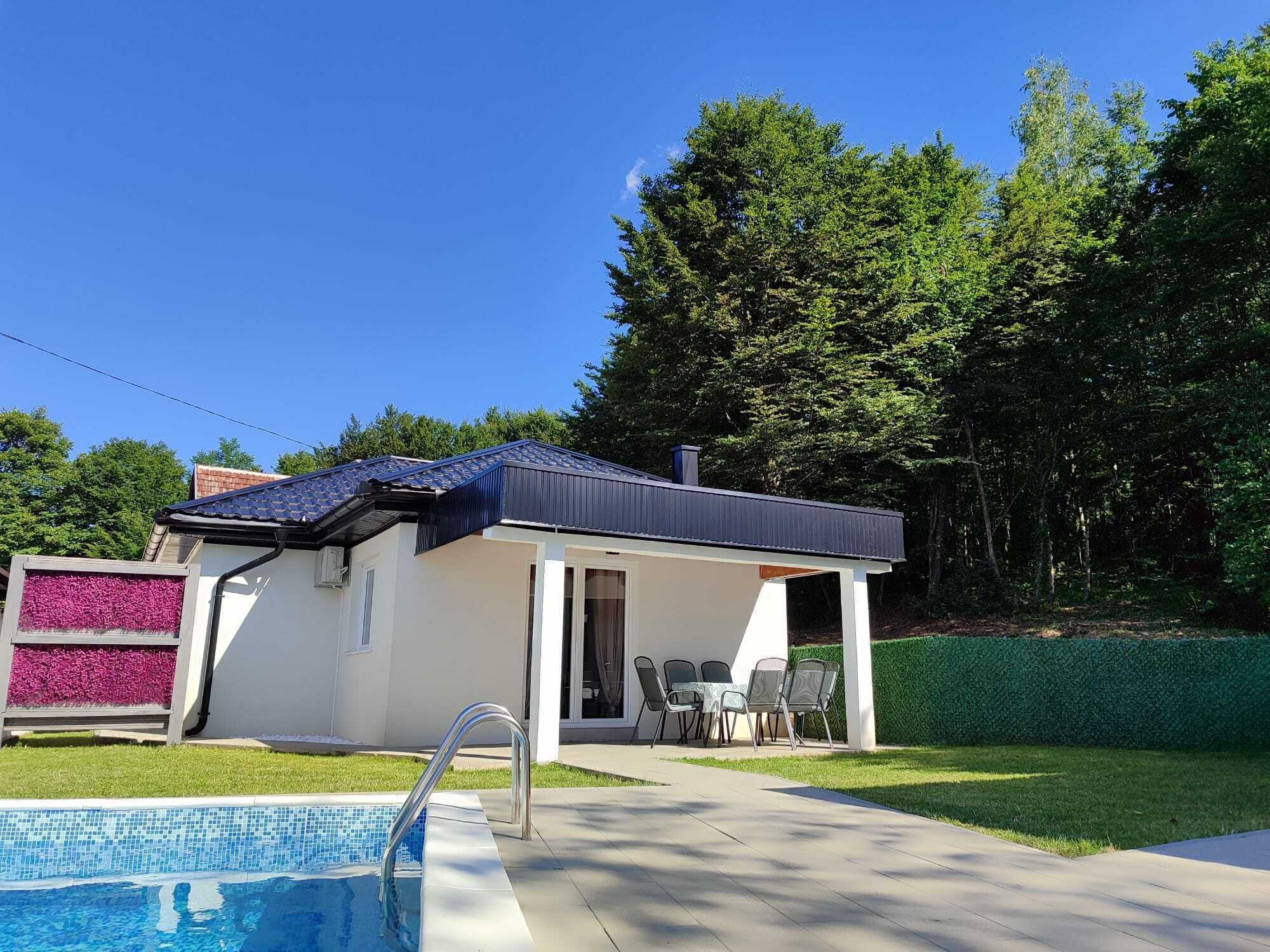 Una casita con piscina, rodeada de un césped cuidado y árboles.