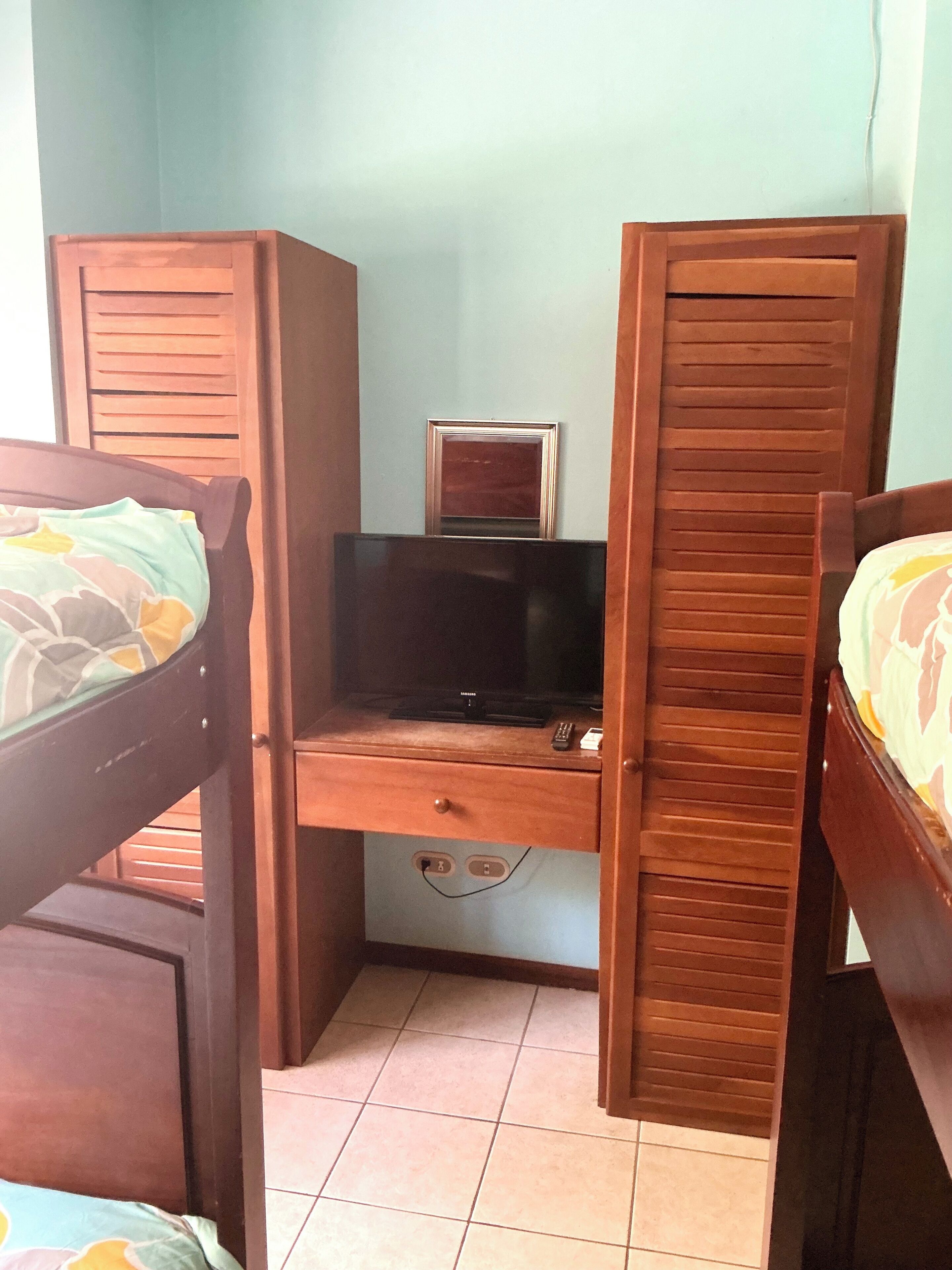Une chambre comprenant un lit, un bureau avec une télévision et un petit placard.