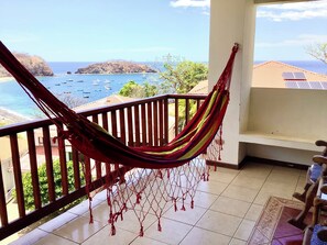 Un hamac sur un balcon donnant sur une plage, avec des bateaux et une île au loin.