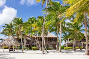 Ett hotell vid stranden med byggnader som har tak av halmtak, palmer och en sandstrand.