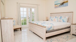 Une chambre à coucher avec un lit en bois, une table de chevet, une commode et une vue sur l’extérieur, visible à travers une porte vitrée.