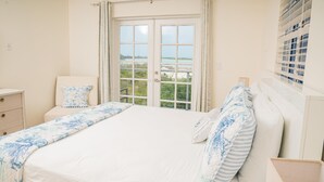 Une chambre à coucher avec un grand lit, une table de chevet, une commode et une fenêtre donnant sur la mer.