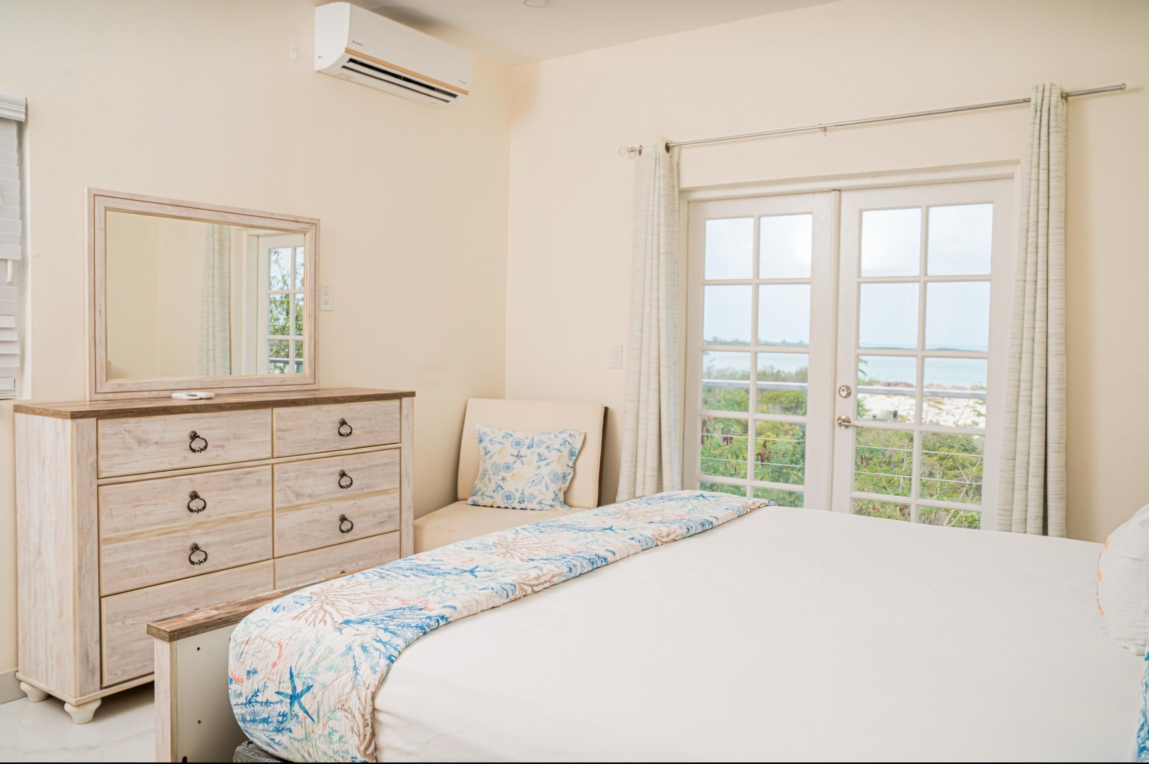 A bedroom with a bed, a dresser, a mirror, and a window with a view.