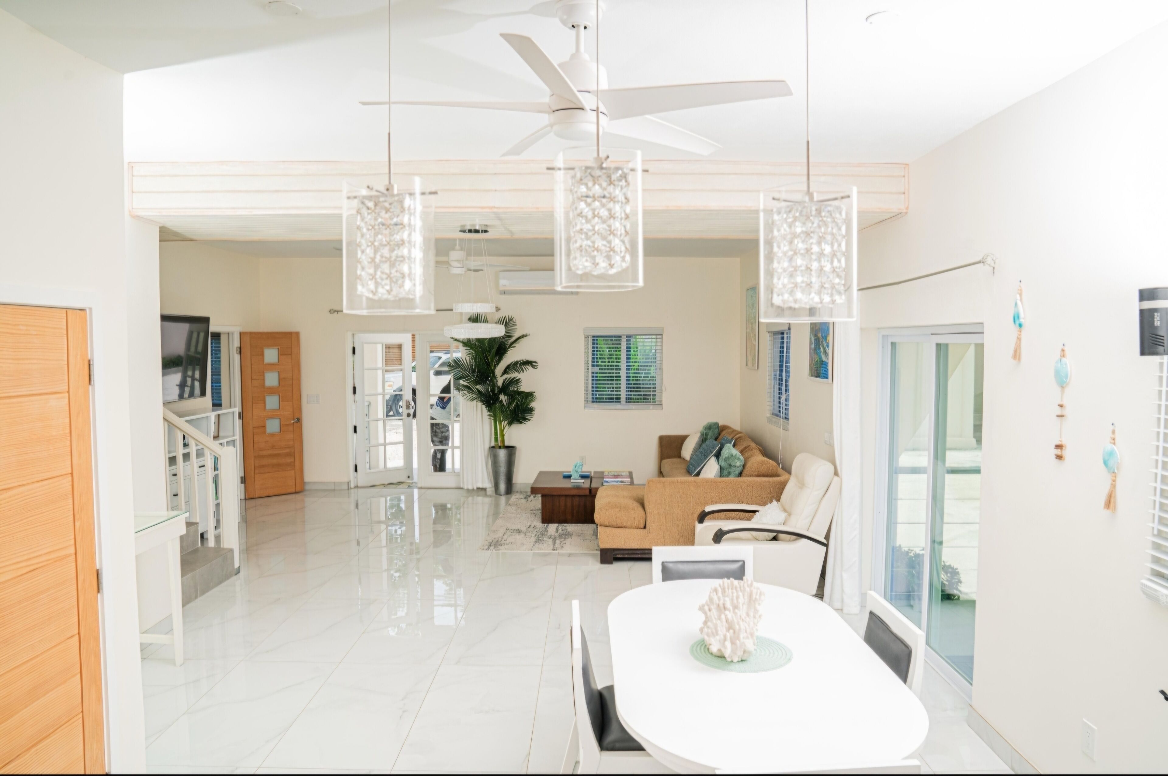 A spacious living area with a white ceiling fan, a dining table with chairs, a sofa, and a potted plant.