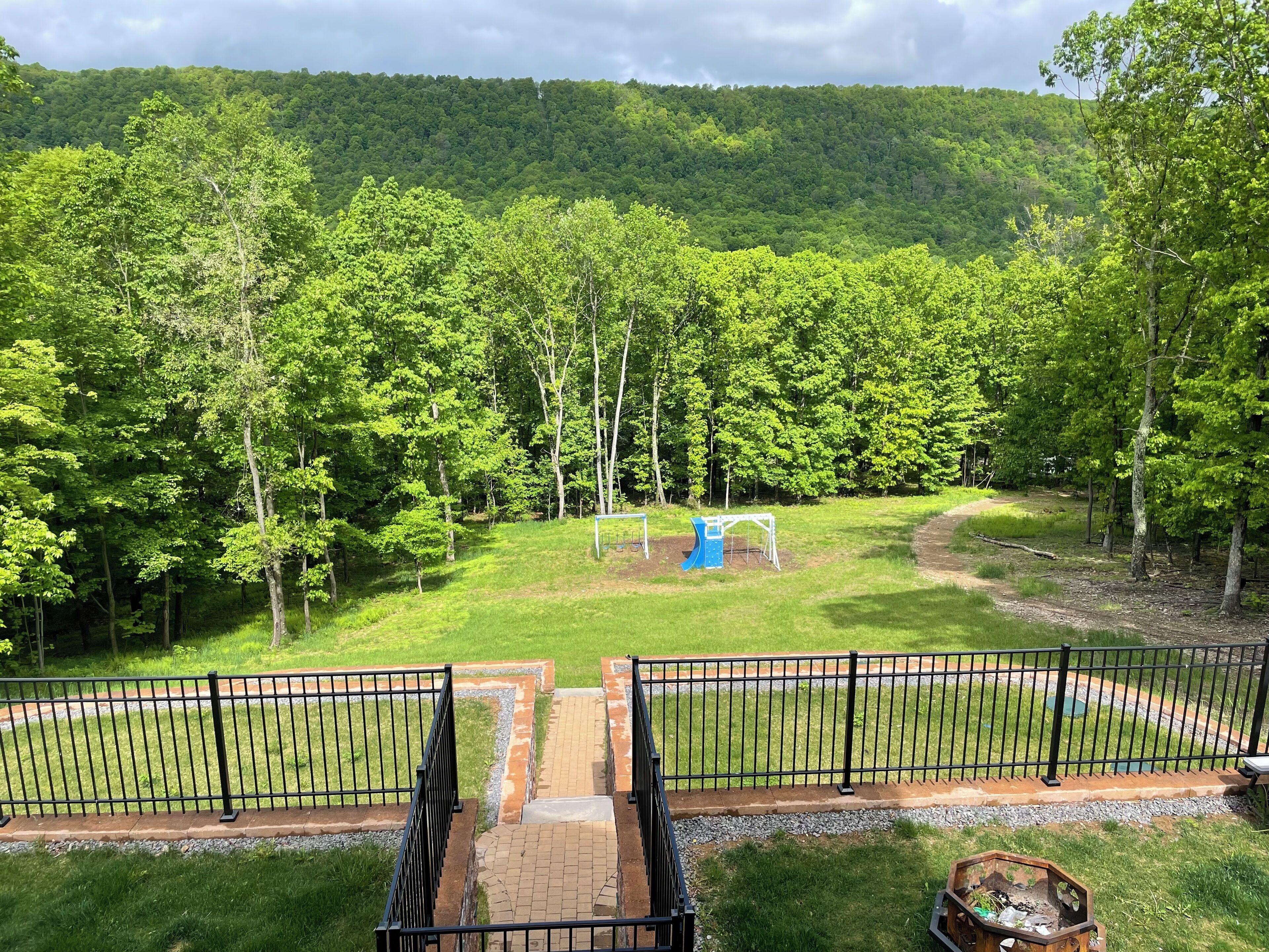 A fenced outdoor area with a playground, surrounded by dense trees and a hilly backdrop.