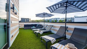 Une terrasse sur le toit, dotée de chaises longues, de parasols à rayures et d’un petit espace salon.