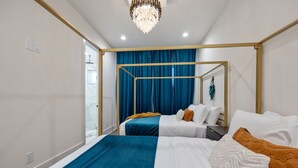 Une chambre d’hôtel moderne avec un grand lit, un lit plus petit et un lit à baldaquin. On y trouve un lustre, une fenêtre et une porte.