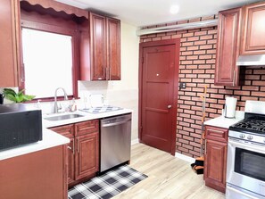 A kitchen with wooden cabinets, a stainless steel dishwasher, a red door, a brick wall, and a stove. - Nice big house with parking, fenced yard (Buffalo)