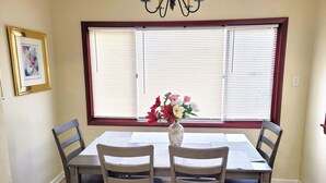 A dining area with a table and four chairs, a vase with flowers, and a window with blinds. - Nice big house with parking, fenced yard (Buffalo)