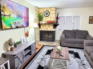A living room with a stone fireplace, a gray sofa, a coffee table, and a large painting on the wall. - Nice big house with parking, fenced yard (Buffalo)