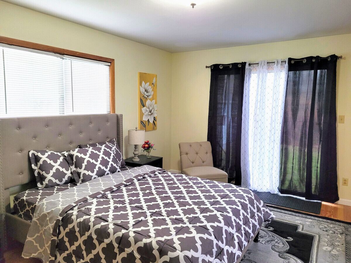A bedroom with a bed, a chair, a nightstand, and a window with curtains.