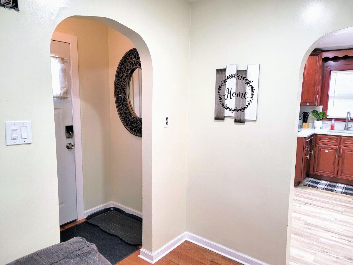 A hallway with a door leading to a kitchen area, a decorative mirror, and a welcome sign.