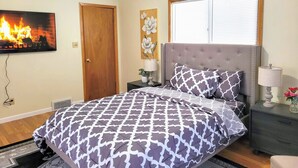 A bedroom with a bed, a nightstand, a wall-mounted TV, a door, and a window with blinds. - Nice big house with parking, fenced yard (Buffalo)