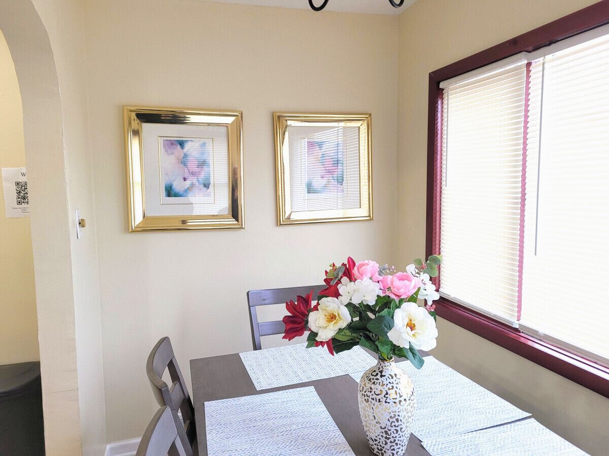 Ein Essbereich mit Tisch für zwei Personen, gerahmten Bildern an der Wand und einer Vase mit Blumen.