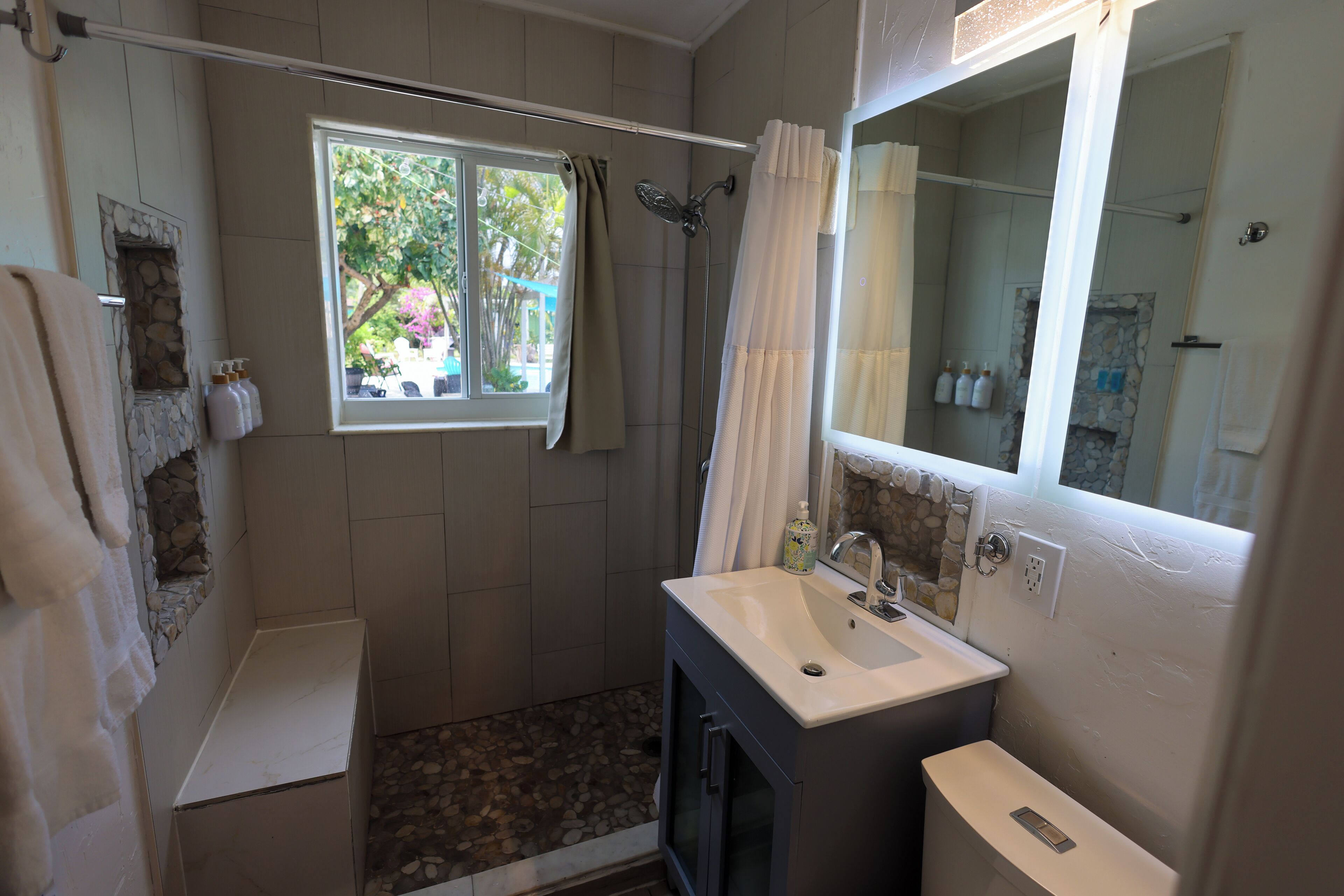 Une salle de bain avec une douche, un lavabo, une fenêtre et un mur en pierre.