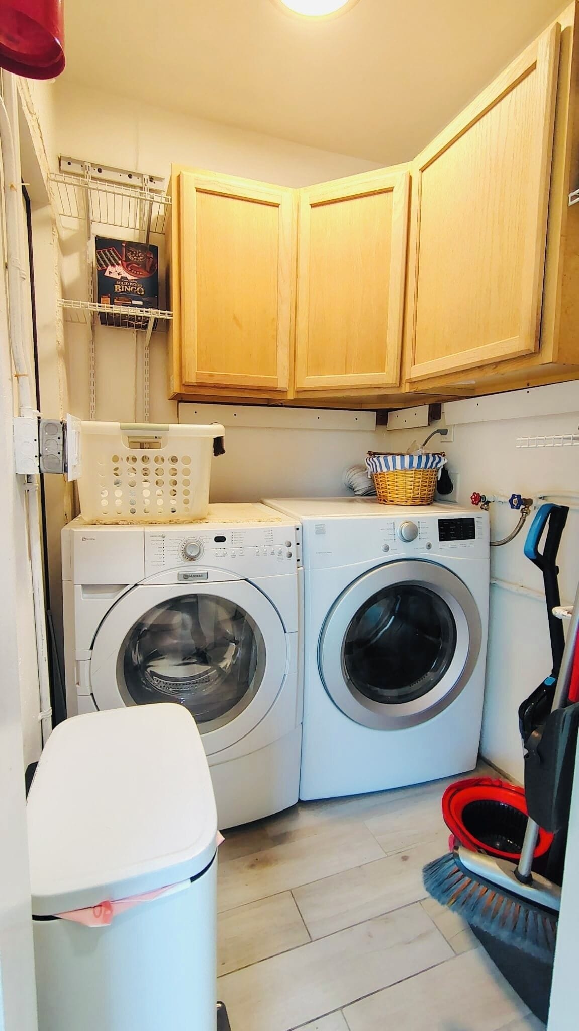 A laundry area with two front-loading washing machines, wooden cabinets, a basket, and a broom.