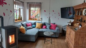 Una sala de estar acogedora con un sofá seccional, una mesita redonda, un mueble de madera y una estufa de leña.