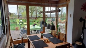 Una mesa de comedor de madera con individuales negros, un banco y vistas al jardín a través de amplios ventanales.